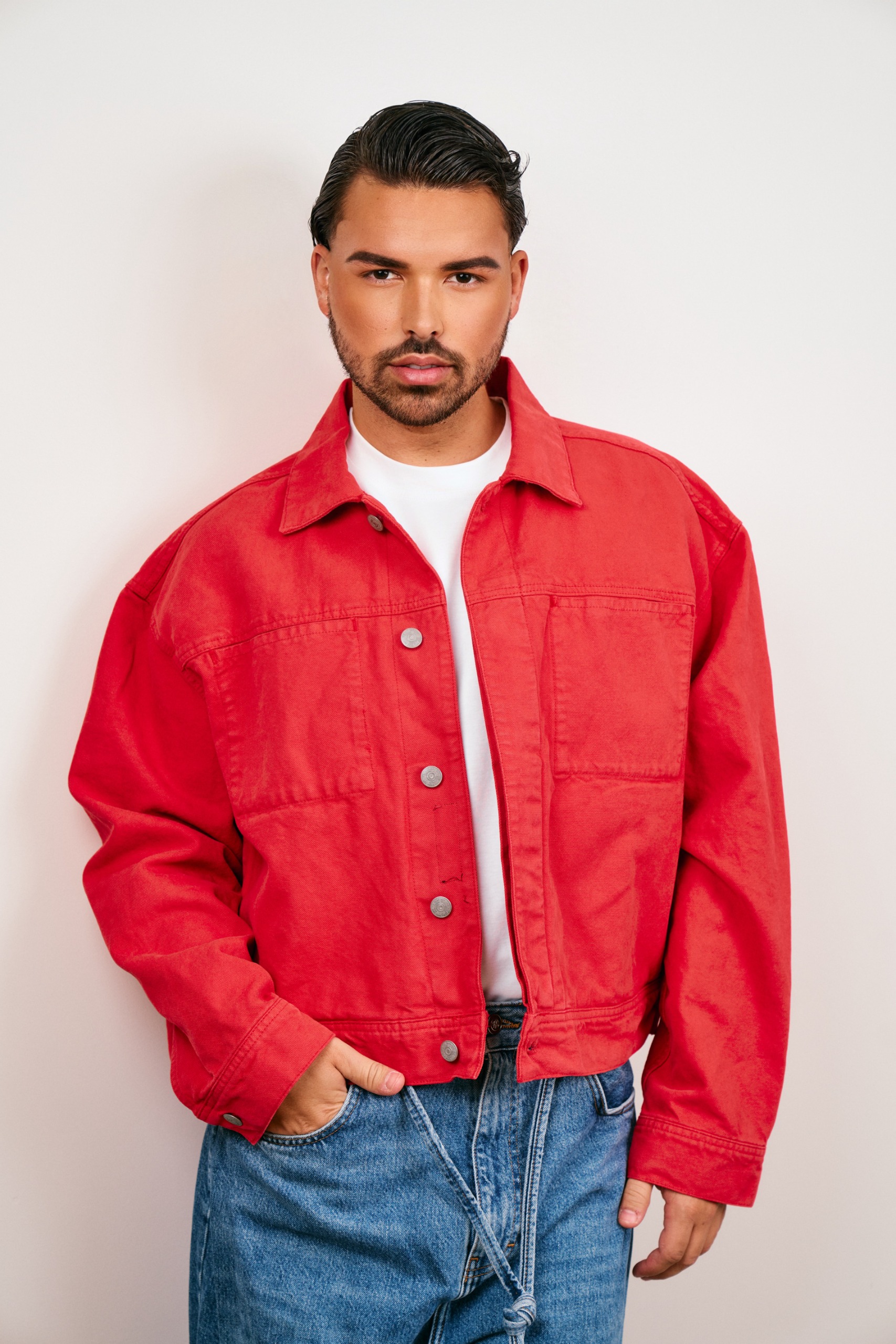 a man with a goatee and dark hair in a red jacket and jeans