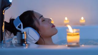 A woman relaxing in the bath as part of her nighttime routine with candles and headphones