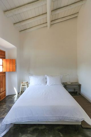 Bedroom with bed with white linen on cement floor with white walls and an open wooden door