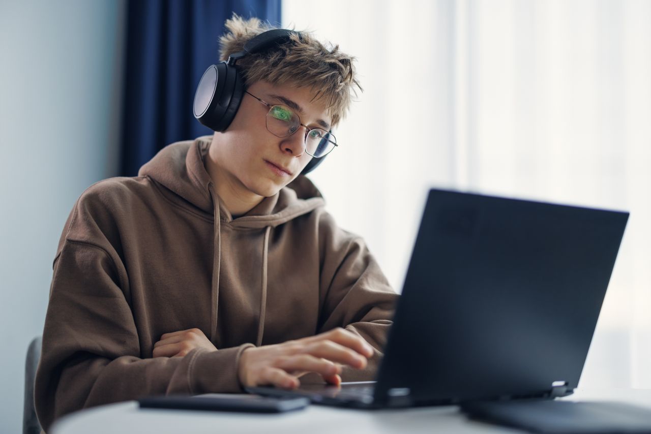 Teenage boy looks at laptop while he sits with headphones on