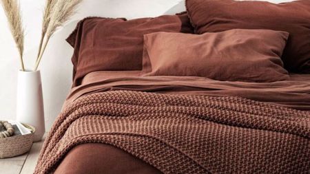 Clay-colored sheets on a bed against a white wall. 