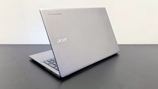 Angled shot of the Acer Chromebook Plus Enterprise 515 facing away, on a black desk against a white background.