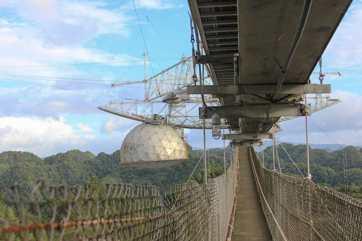 An image shows the catwalk astronomers used to reach the science equipment, including a radar transmitter, suspended over the massive radio telescope at Arecibo Observatory.