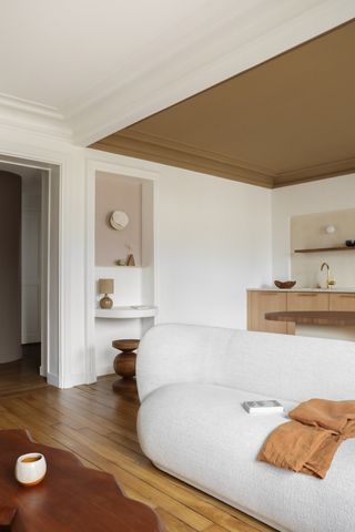 A living room with a white boucle sofa and a brown painting ceiling