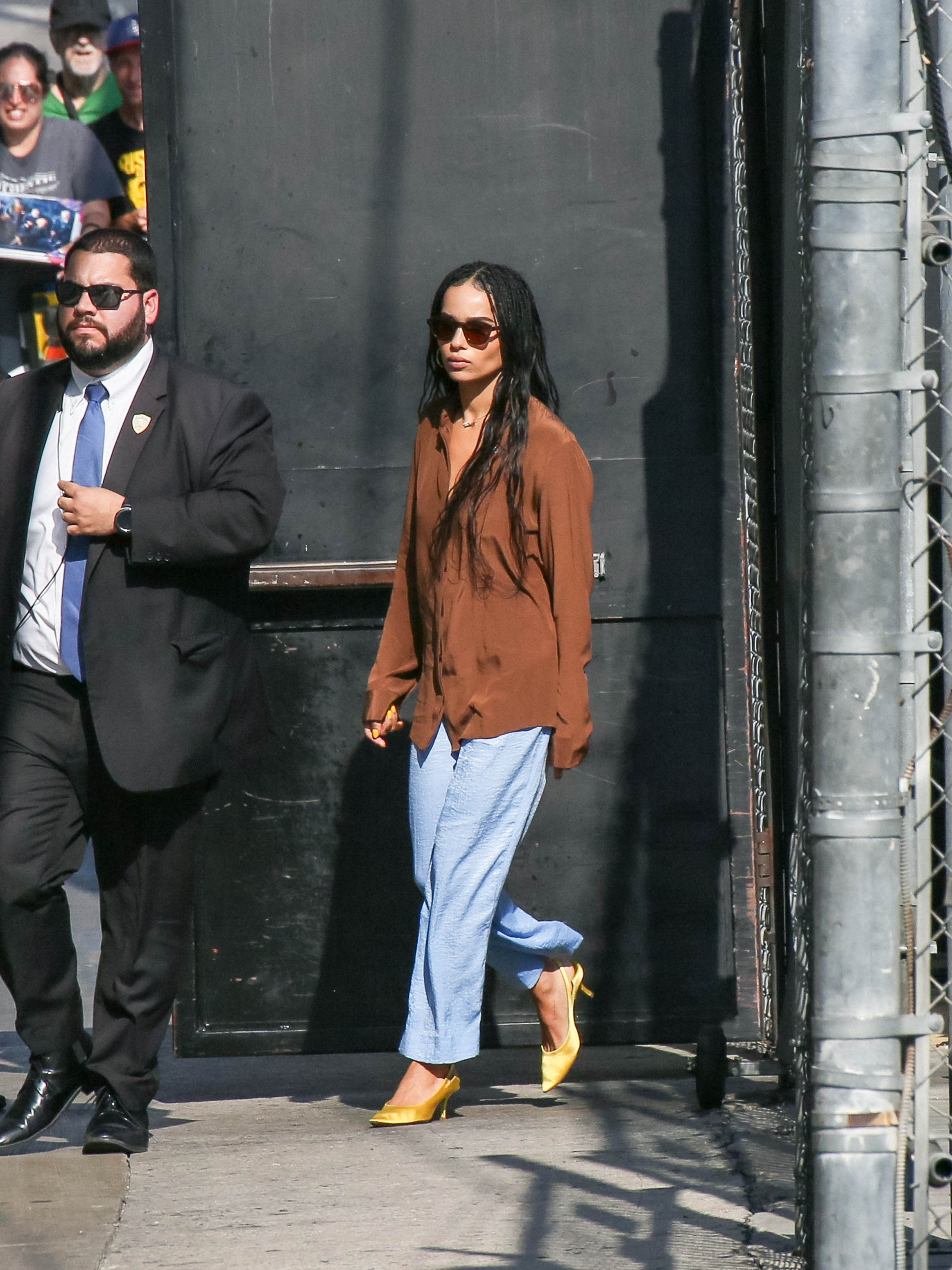 Zoe Kravitz wears a brown shirt with blue trousers.