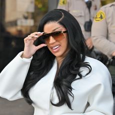 a paparazzi photo of a woman with black hair wearing a white pantsuit and brown sunglasses