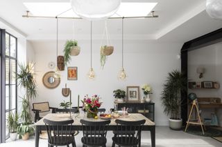 Dining area with black table and chairs with pine top, pendant lights suspended overhead by a rod under a rooflight