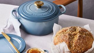 A pale blue Le Creuset Dutch Oven with a pale blue Le Creuset plate with a loaf of sourdough in front of it