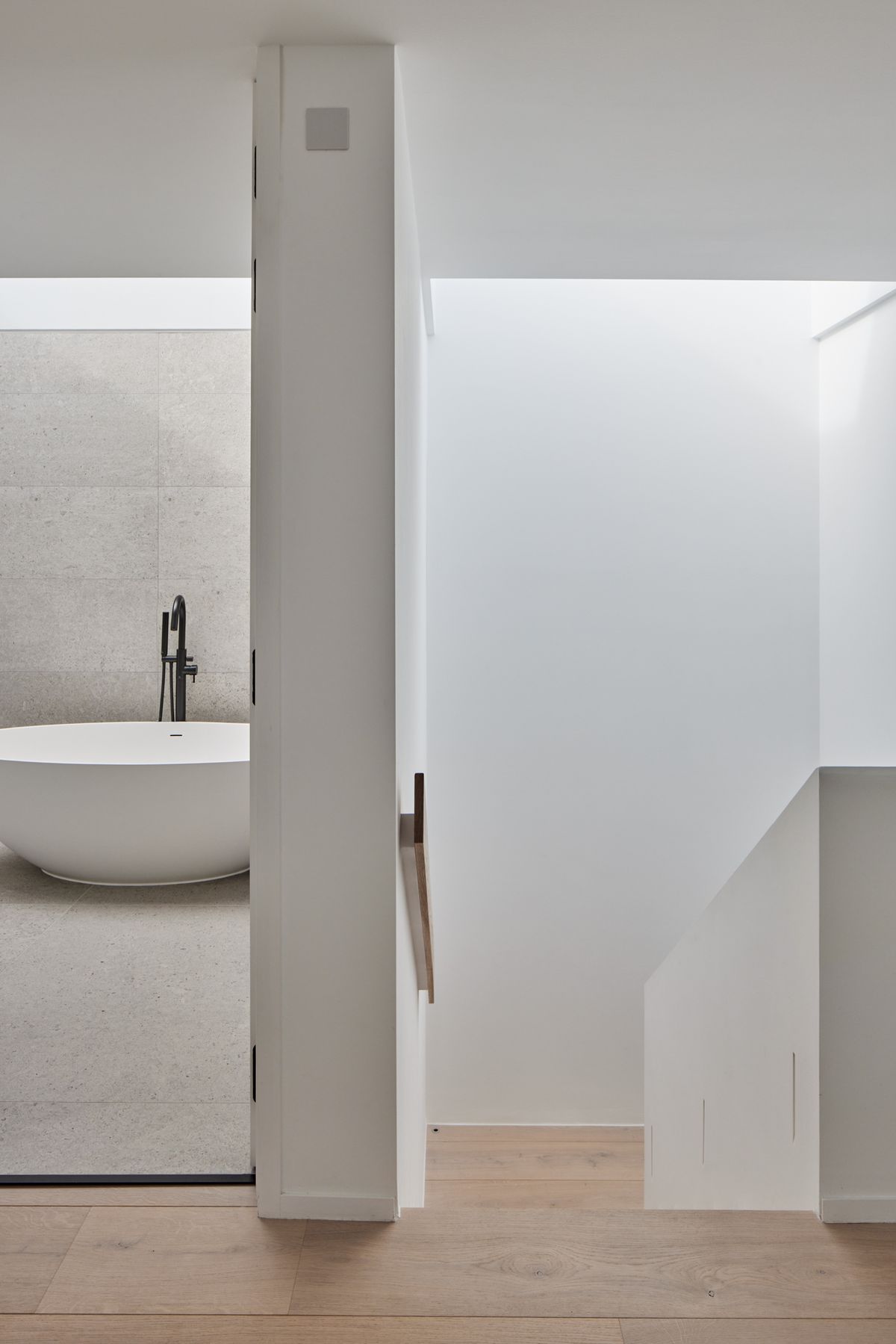 A view of a modern landing with one doorway open to reveal a minimalistic bathroom and a stairway leading downstairs
