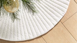 A white velvet tree skirt on a wooden floor