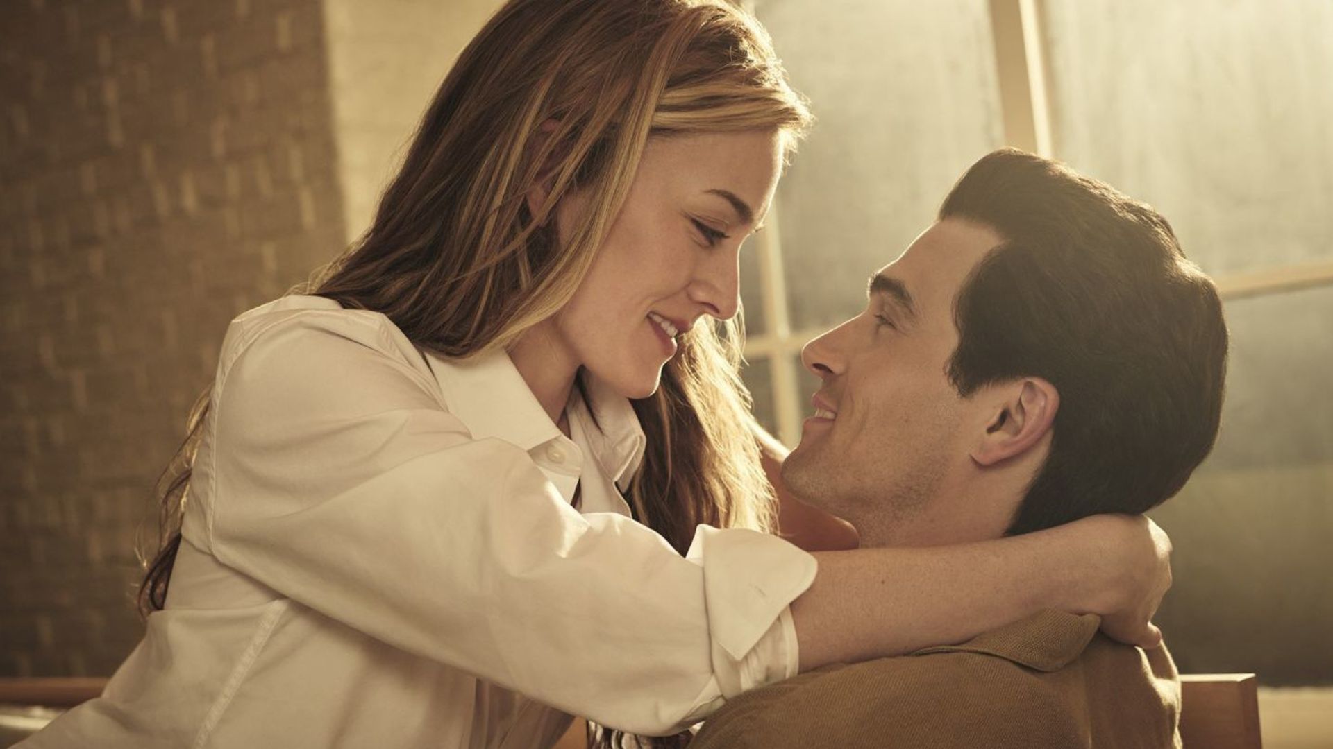 Caroline sits on John's lap with her arms around his neck