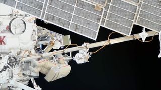 two cosmonauts in white spacesuits work outside the international space station