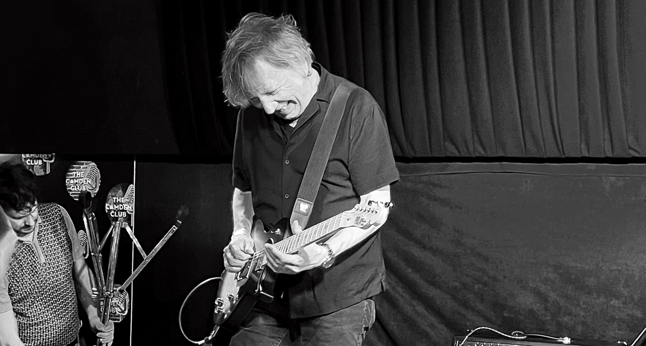 A black and white action shot of Dave Burrluck performing onstage