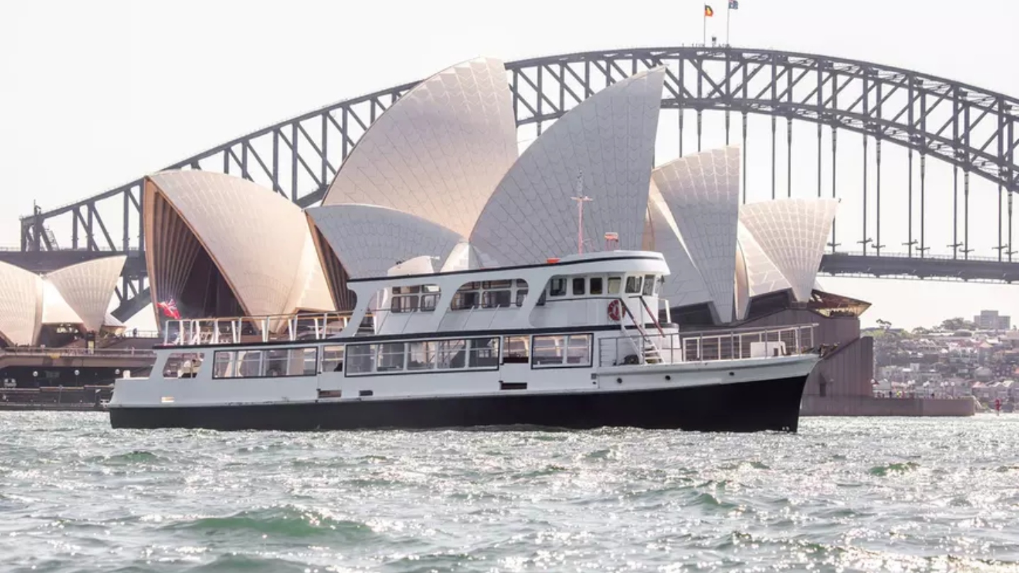 A white boat in Sydney Harbour in front of the Opera House and Sydney Harbour Bridge