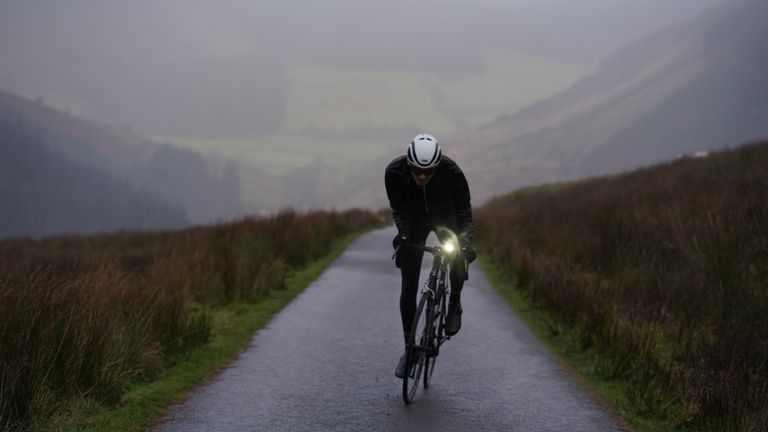 Best winter cycling jackets image shows a rider head on wearing a helmet and winter cycling clothing and on a black bike riding on the road. 