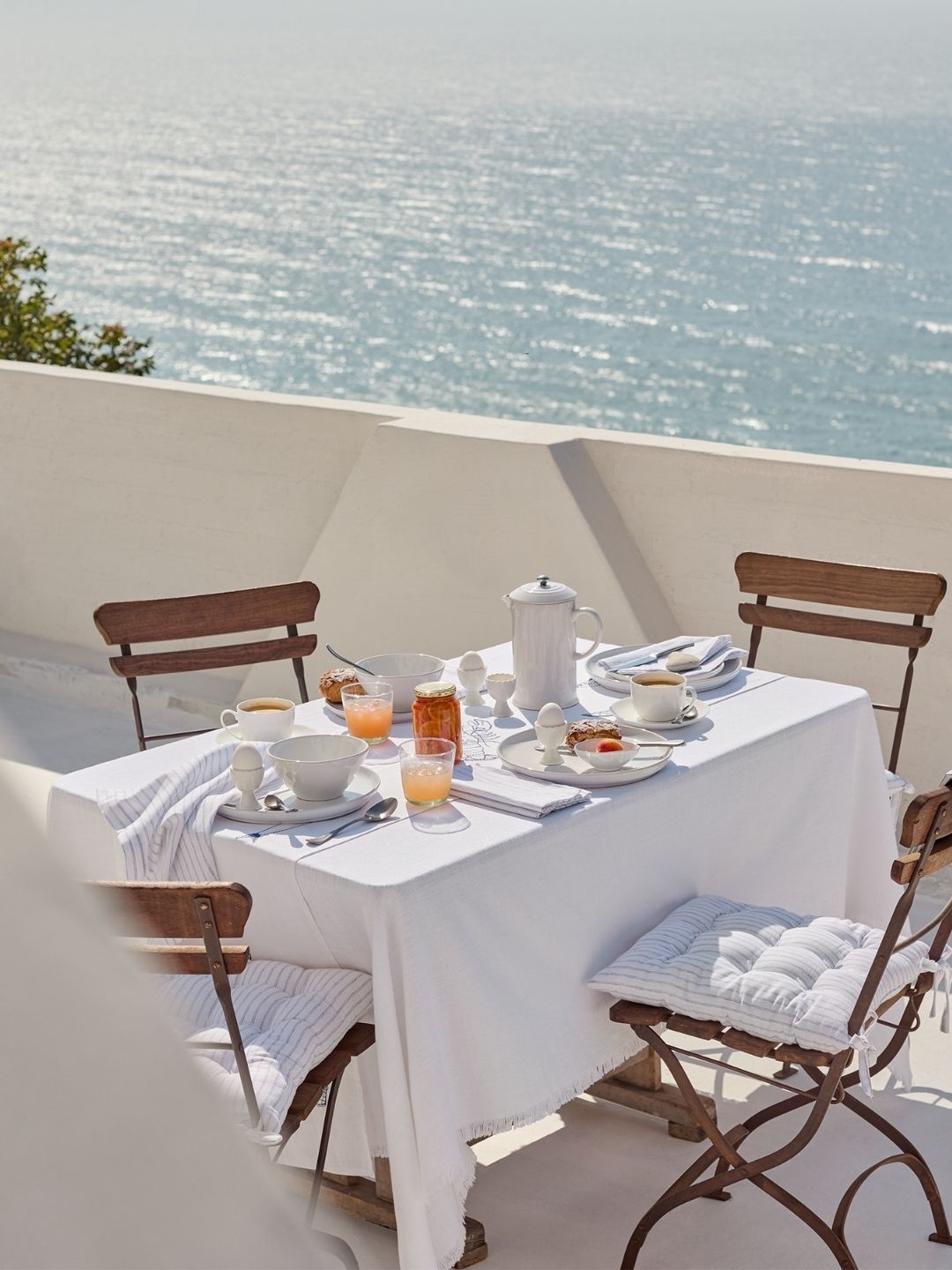 Image of  a white table setting on a white patio in front of the sea.