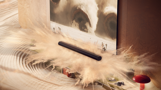 A stylised image of the Sonos Arc Ultra soundbar in a living room, with sand exploding from the speakers