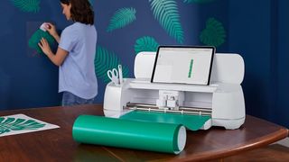 The best Cricut machines; a photo of a Cricut Maker 3 on a table as a woman makes wallpaper