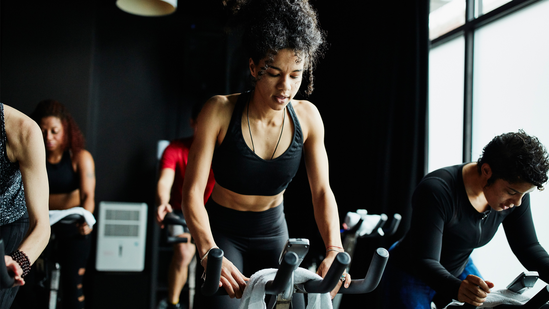 How often should you work out? Image of woman riding exercise bike in spin class gym