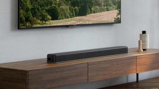 En svart Sony HT-X8500 Soundbar ligger på en träfärgad TV-bänk