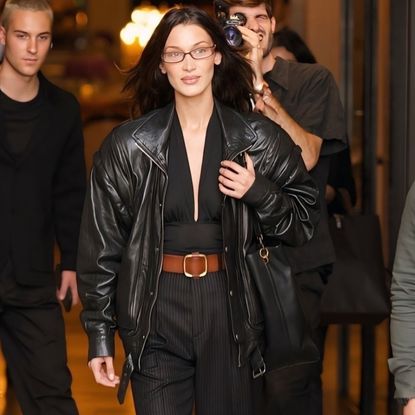 Bella Hadid wears a black aviator jacket and a plunge top on her way to the saint laurent show