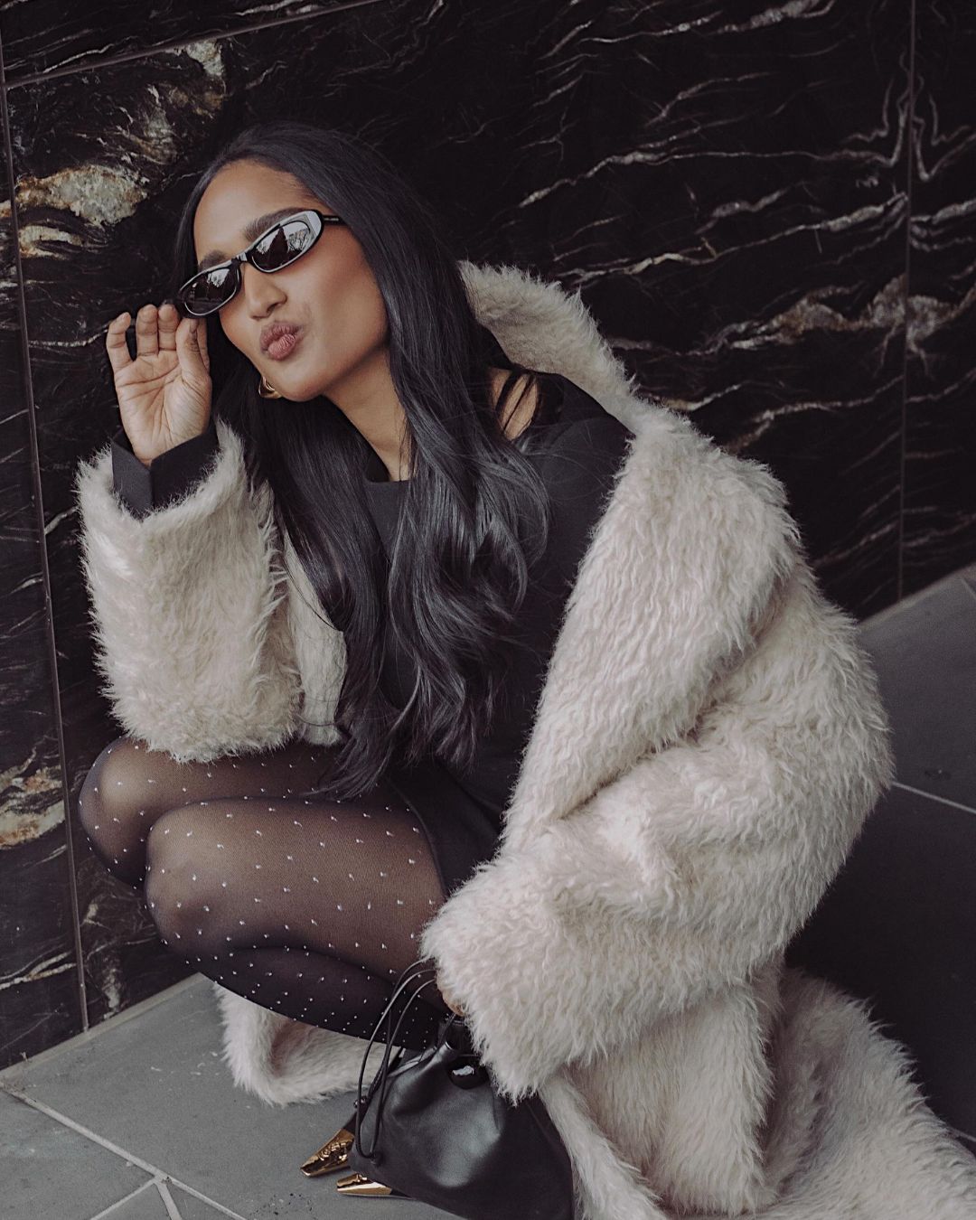 Influencer @divrav wears patterned polkadot tights with a fur jacket and black dress.