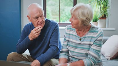 An older couple sit on the sofa and have a serious discussion.