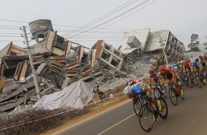 The peloton passes ruined buildings on stage 3