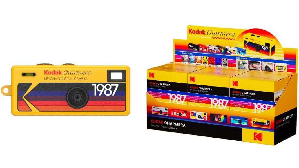 A studio shot of a yellow Kodak Charmera on white, positioned next to a box of six unopened Charmera cameras in their vintage 35mm film-styled packaging