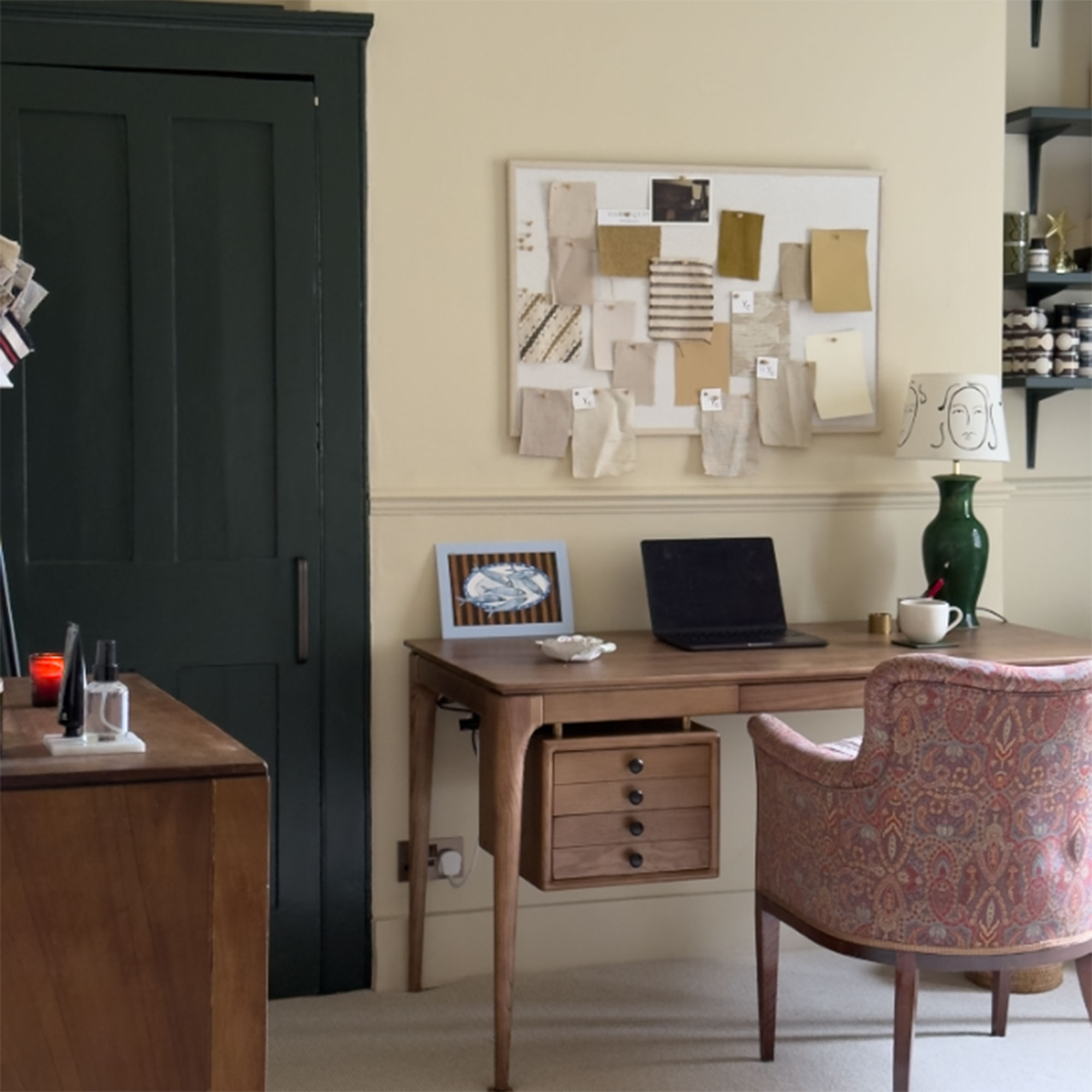 Neutral home office with wooden desk, patterned upholstered armchair and pinboard on wall above desk showing fabric samples