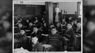 Cree students at their desks with their teacher in a classroom at All Saints Indian Residential School, in Lac La Ronge, Saskatchewan, March 1945.