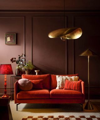 living room with gold pendant and floor light, red table lamp, orange sofa and light maroon walls