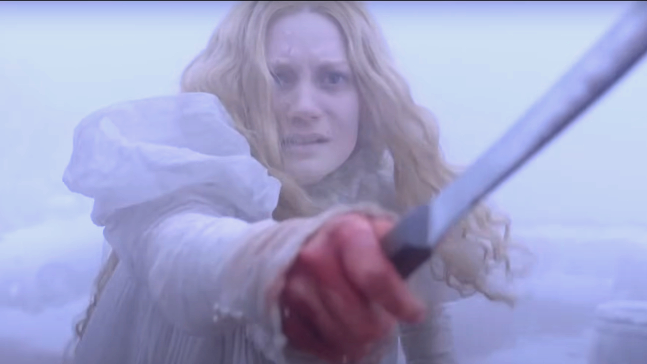 Una asustada Mia Wasikowska sostiene una espada en su mano ensangrentada en Crimson Peak.