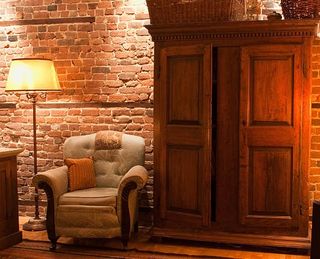 Old wooden wardrobe next to an armchair against a bare red brick wall