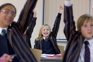 children in blazers raising their hands - what to look out for when buying a school uniform