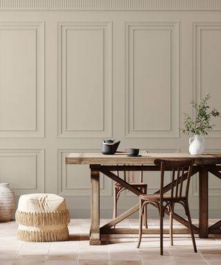 large cream wall mural with traditional wall panelling design, wooden dining table in front with chairs and cream floor pouffes to side