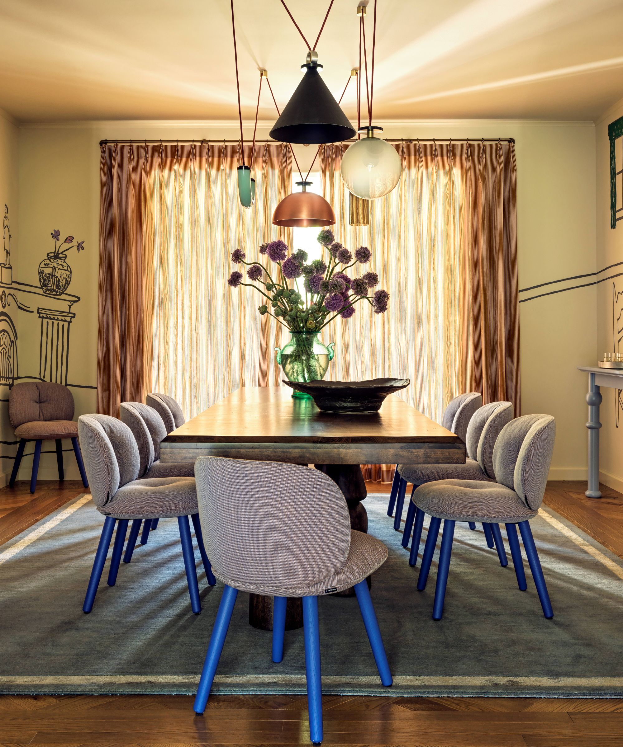 Dining room with painted mural, large wooden table and grey and electric blue dining chairs