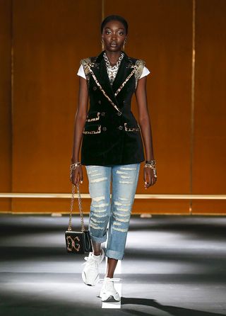 Lady wearing blue ripped jeans, a black and leopard print waistcoat, D & G logo bag and jewellery