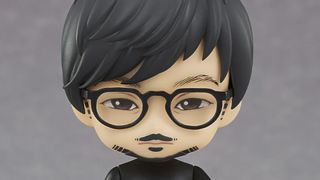 Hideo Kojima Nendoroid figure against a gray background, staring into the foreground