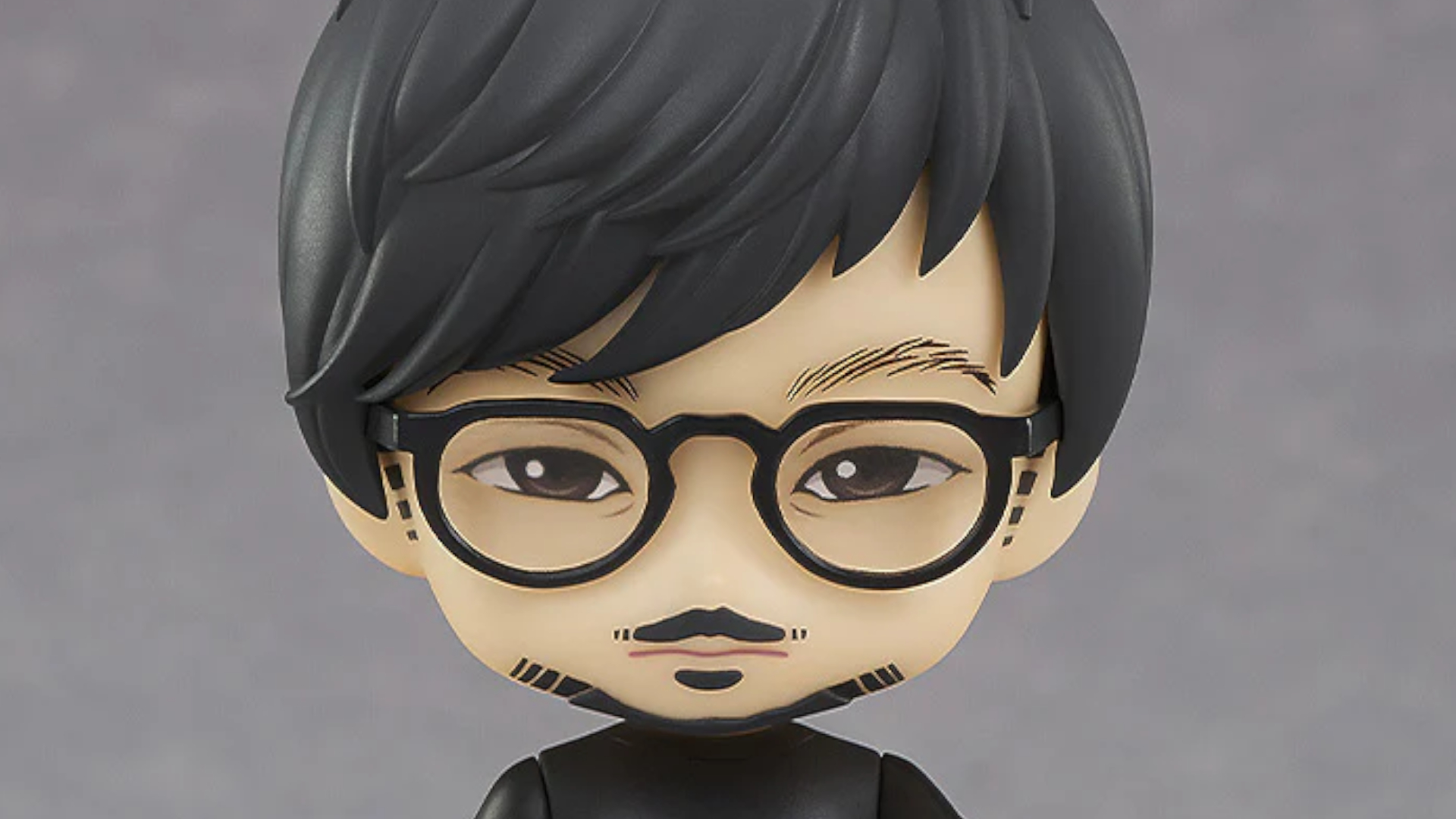 Hideo Kojima Nendoroid figure against a gray background, staring into the foreground