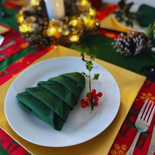 Green napkin in Christmas tree shape with berries on a white plate and yellow placemat