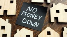 The words "no money down" written in white on a black note in the center of wooden cutouts of houses.