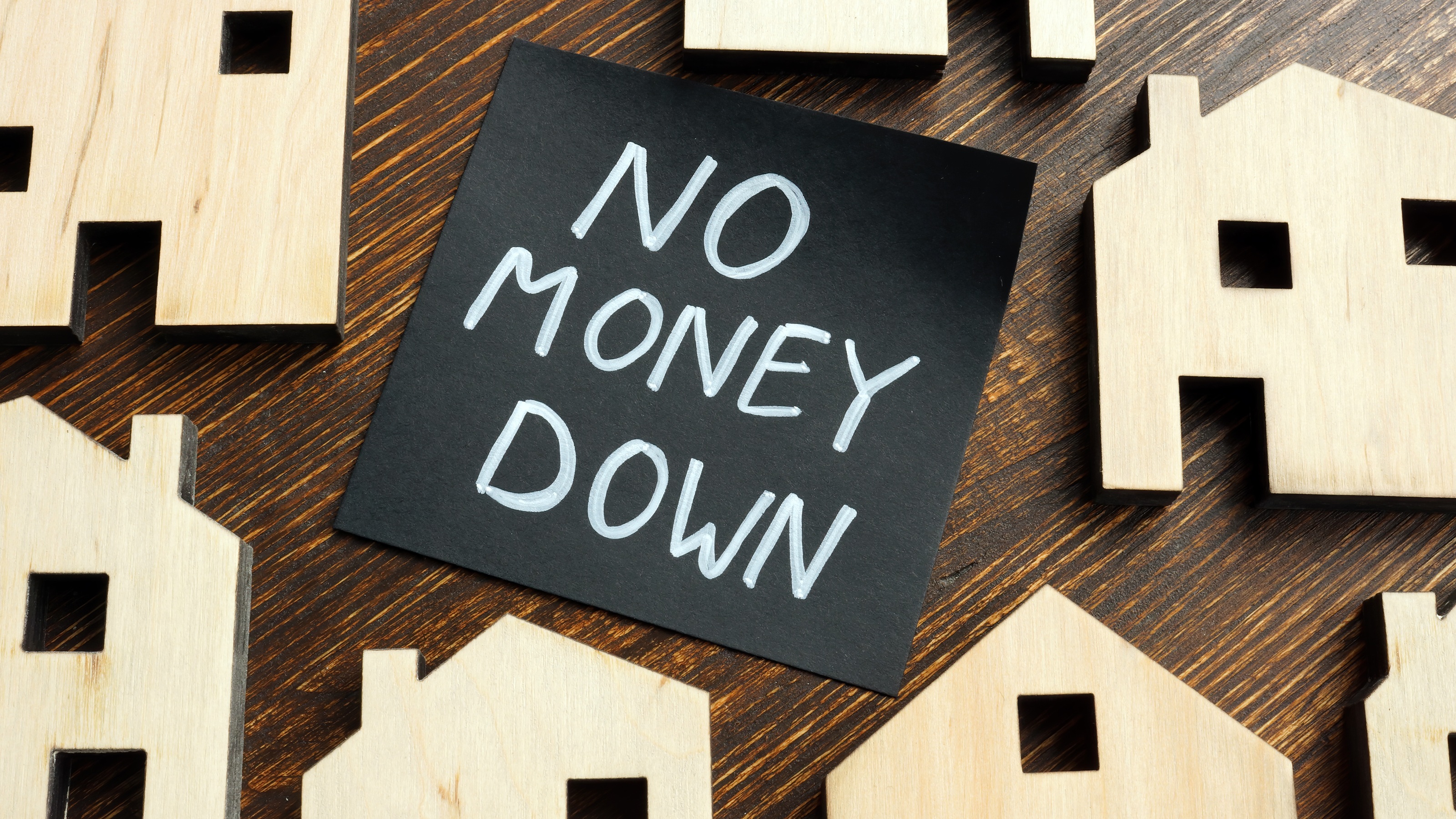 The words "no money down" written in white on a black note in the center of wooden cutouts of houses.