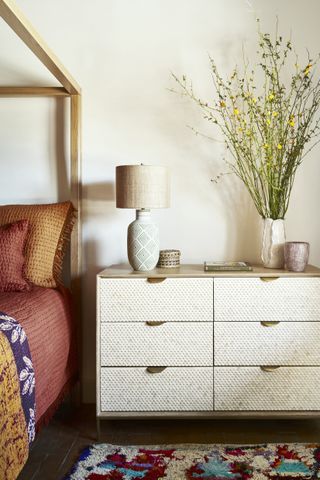 bedroom with nightstand and four poster bed, tall flowers on nightstand, quilted bedding, tufted rug, vases and table lamp