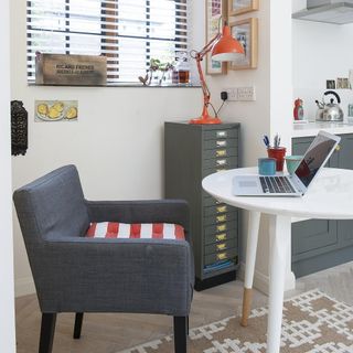Home office next to kitchen with round table, grey chair and filing cabinet