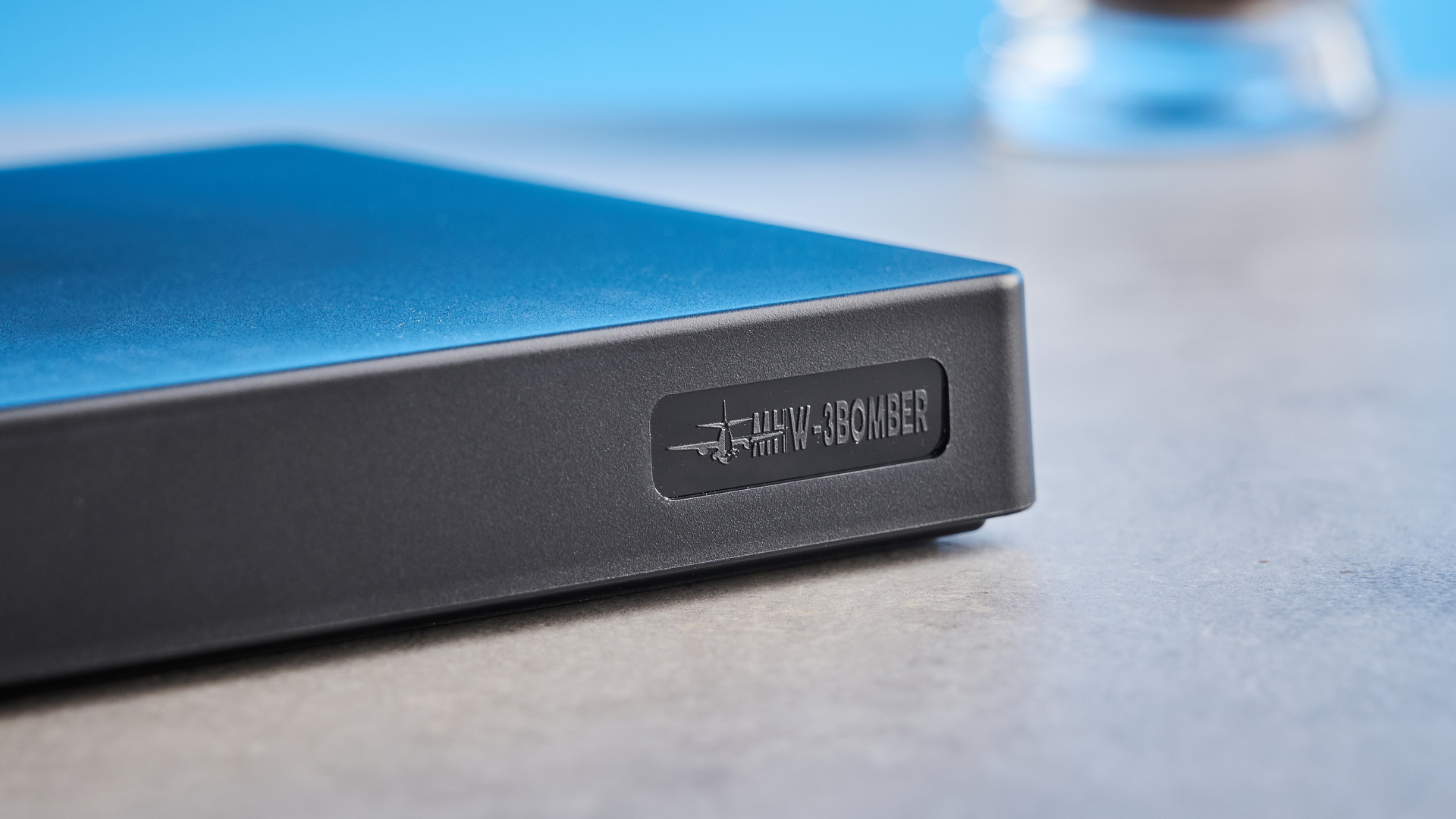 the mhw-3bomber cube coffee scale 2.0 in black photographed against a blue background showing its button controls and dial surface