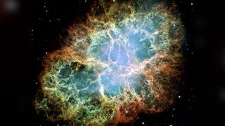 Hubble Space Telescope image of the Crab Nebula shows a large cloud of gas and dust colored orange, yellow and a lighter pink and blue toward the center.