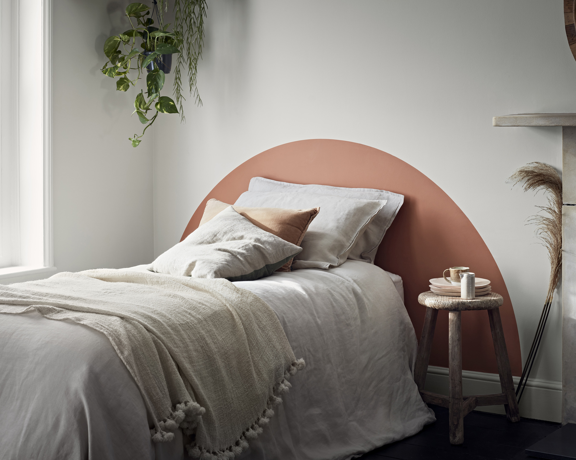 A neutral bedroom with white walls and bedlinen and a terracotta painted headboard.