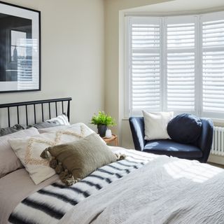 Neutral painted bedroom with black headboard and neutral bedding, navy armchair