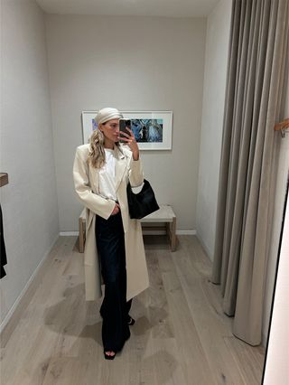 Eliza Huber in the dressing room at Banana Republic wearing a white sleeveless T-shirt with wide-leg dark-wash denim, a headscarf, a black mini bag, a tan jacket, and black flat slides.